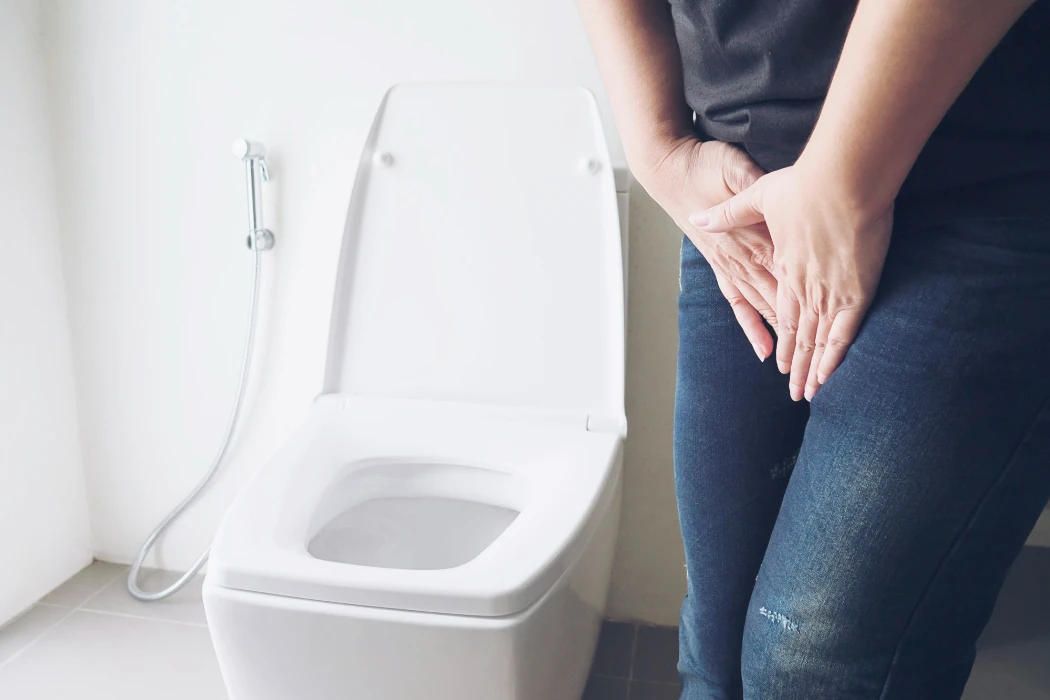 A woman holding her bladder stood next to a toilet